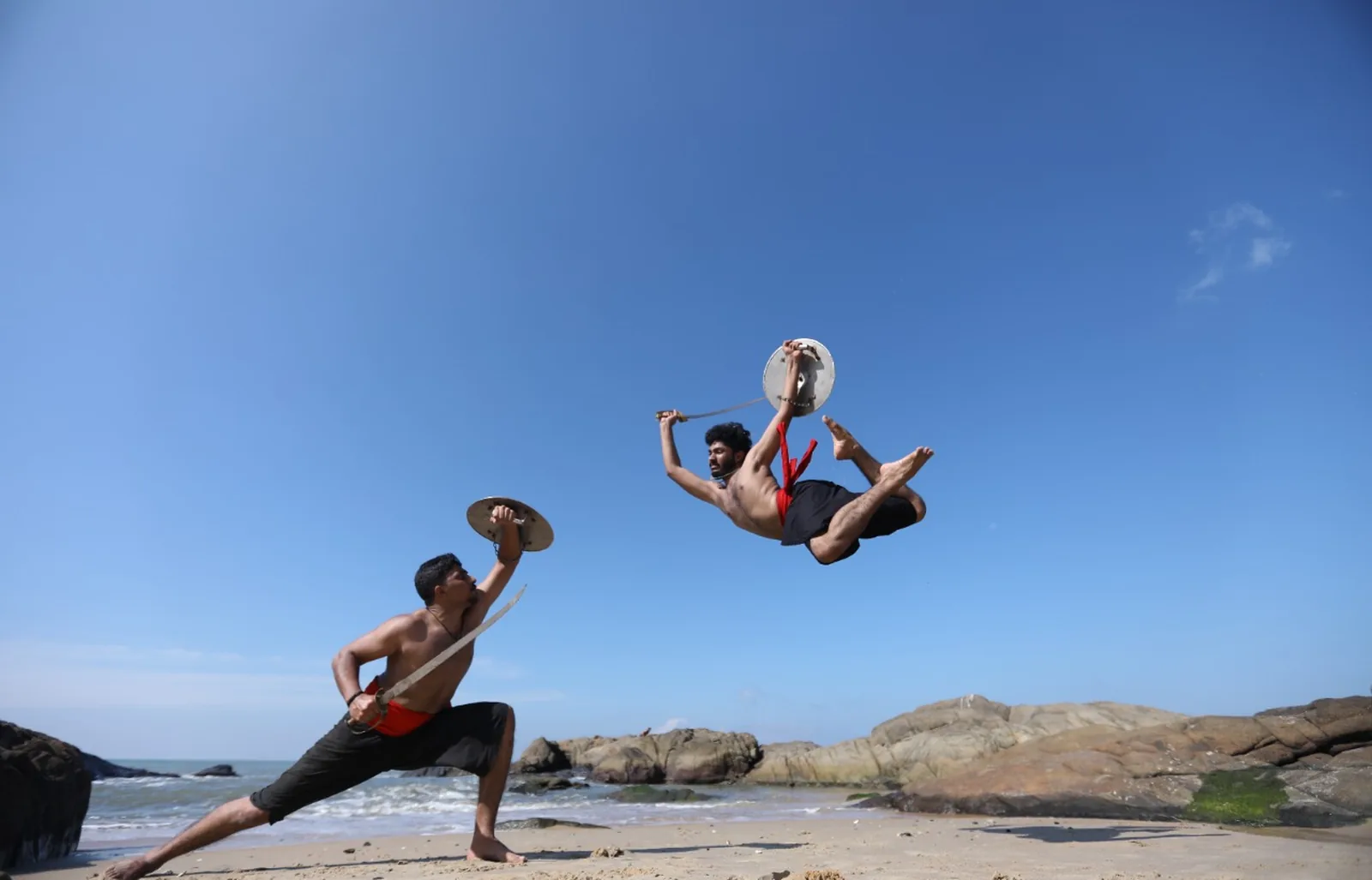 Kalaripayattu warriors leaping with sword and shield on a beach