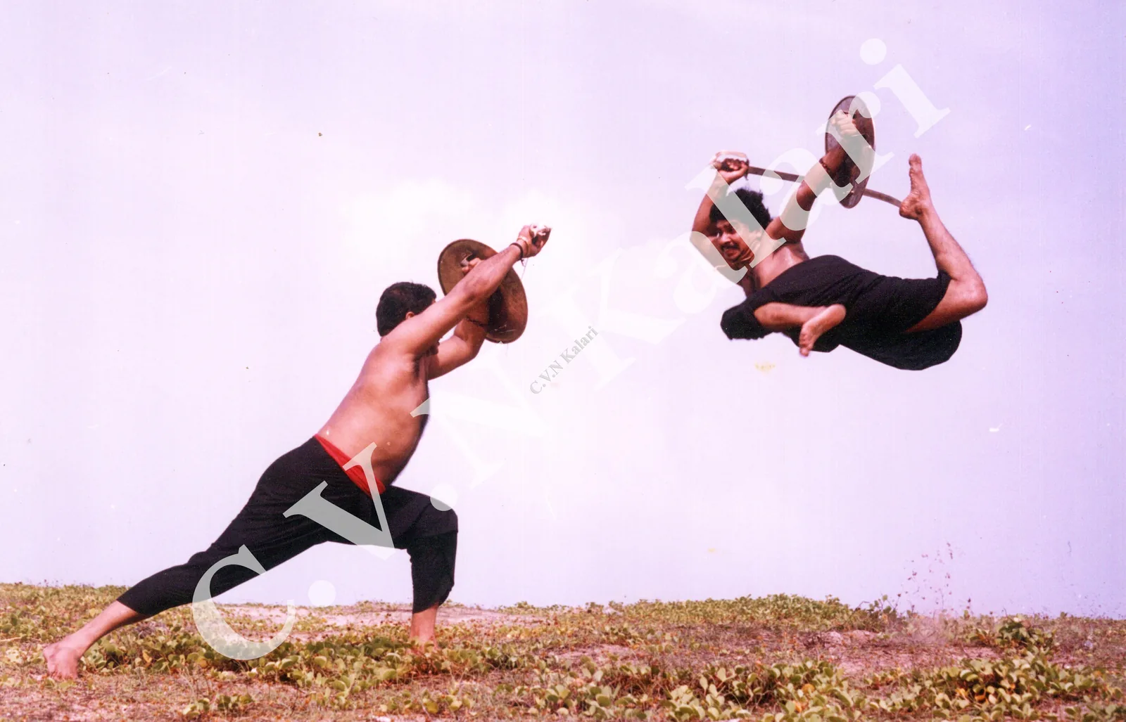 Classic CVN Kalari photograph of a sword-and-shield flying kick